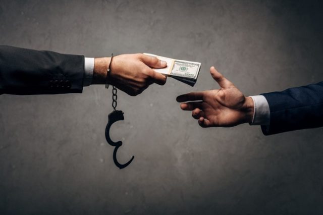cropped view businessman in handcuffs giving bribe to business partner on grey